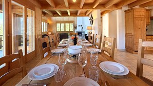 Comedor de madera con una larga mesa dispuesta para una comida, vigas de madera en el techo y ventanas grandes.