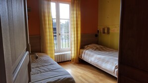 Ein kleines Zimmer mit zwei Einzelbetten, einem Fenster mit gelben Vorhängen und einem Heizkörper darunter.