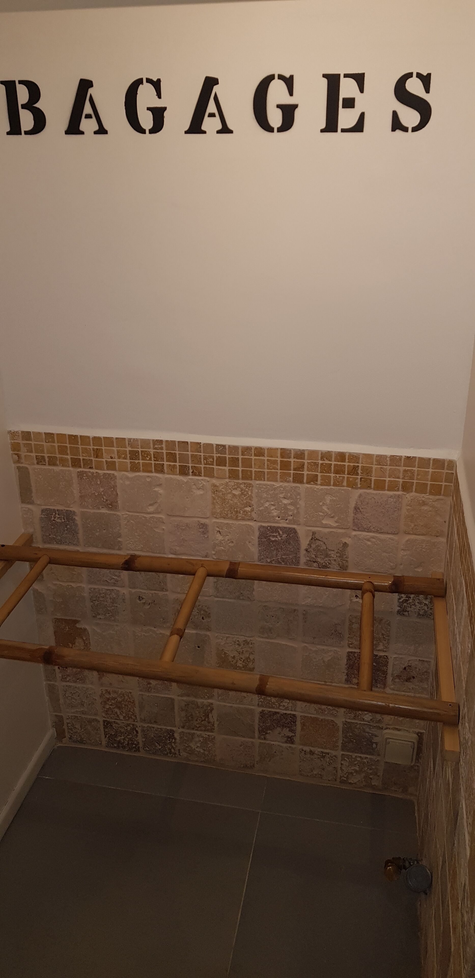 A bathroom with a tiled wall, a bamboo ladder, and the word "BAGAGES" on the wall.