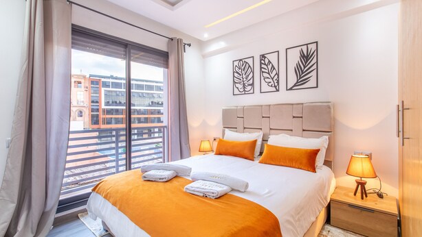 Habitación de hotel con una cama grande, dos lámparas de noche, vistas a edificios a través de la ventana y obras de arte en la pared.