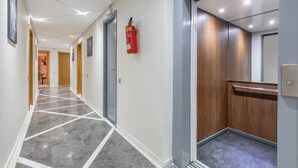 Un pasillo moderno con piso de mármol, puertas de madera y un extintor de incendios montado en la pared.