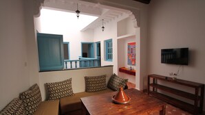 Uma sala de estar aconchegante com uma mesa de madeira, almofadas estampadas e uma televisão sobre um suporte de madeira.
