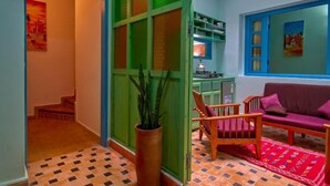 Um corredor com divisória verde, uma cadeira de madeira, um sofá roxo e um tapete vermelho.