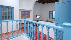Um quarto com corrimão azul, tapete vermelho estampado e uma televisão na parede.