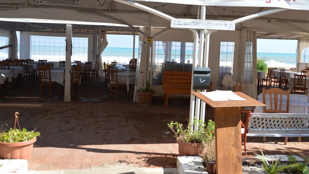 An outdoor dining area with tables and chairs, a wooden bench, and potted plants. - Il Veliero (Pachino)