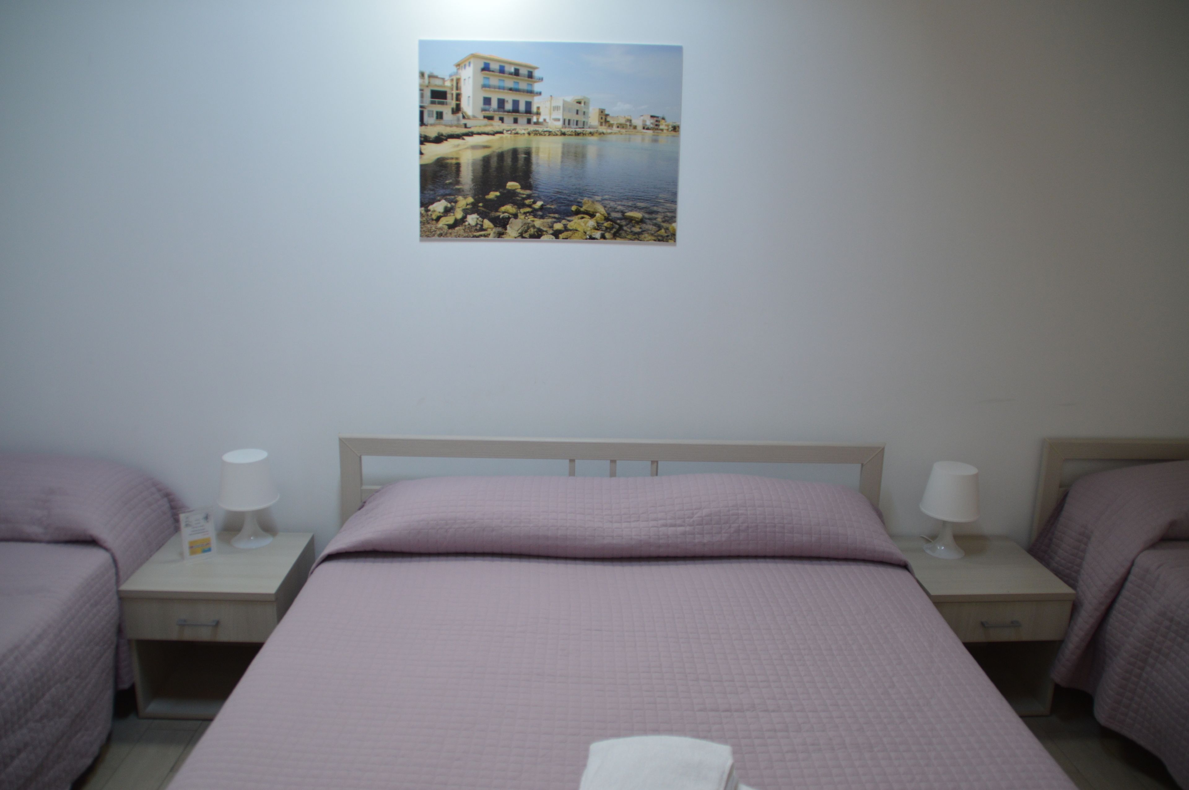 A hotel room with a single bed, two bedside tables, and a wall-mounted picture of a coastal scene.