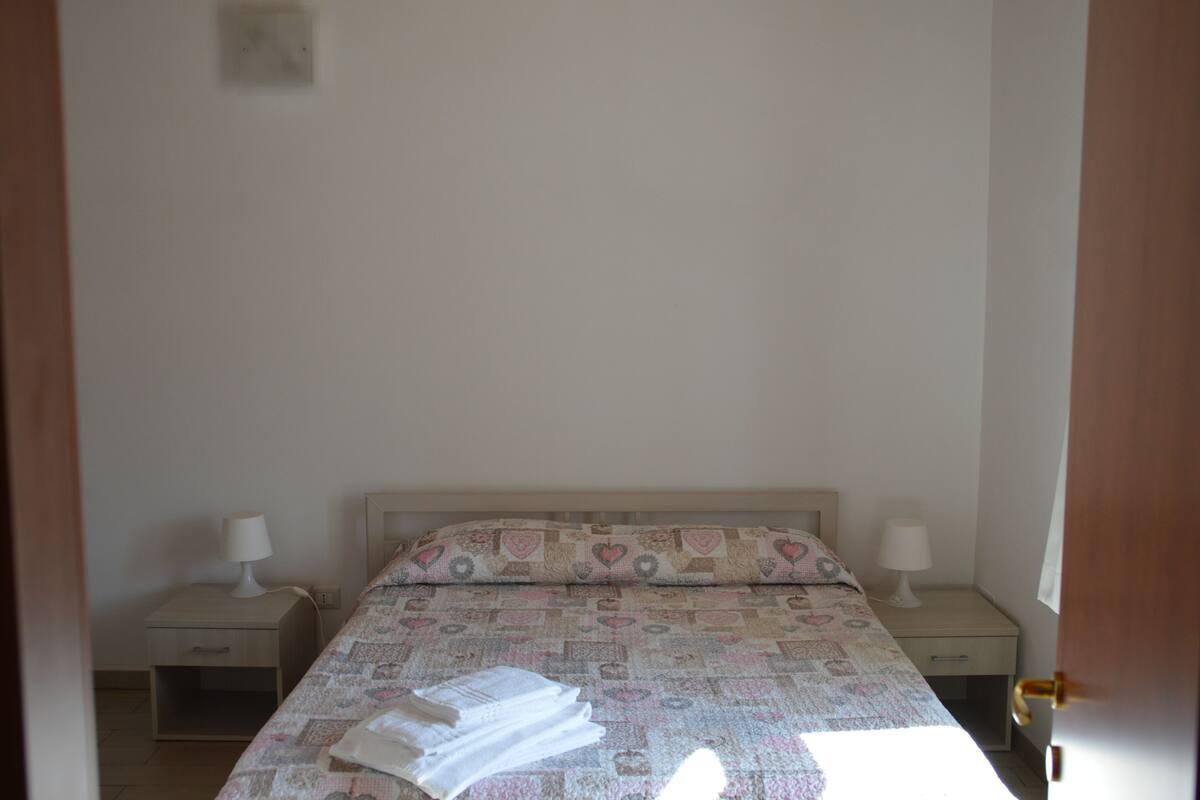 A simple, clean bedroom with a bed, two bedside tables, and a nightstand.