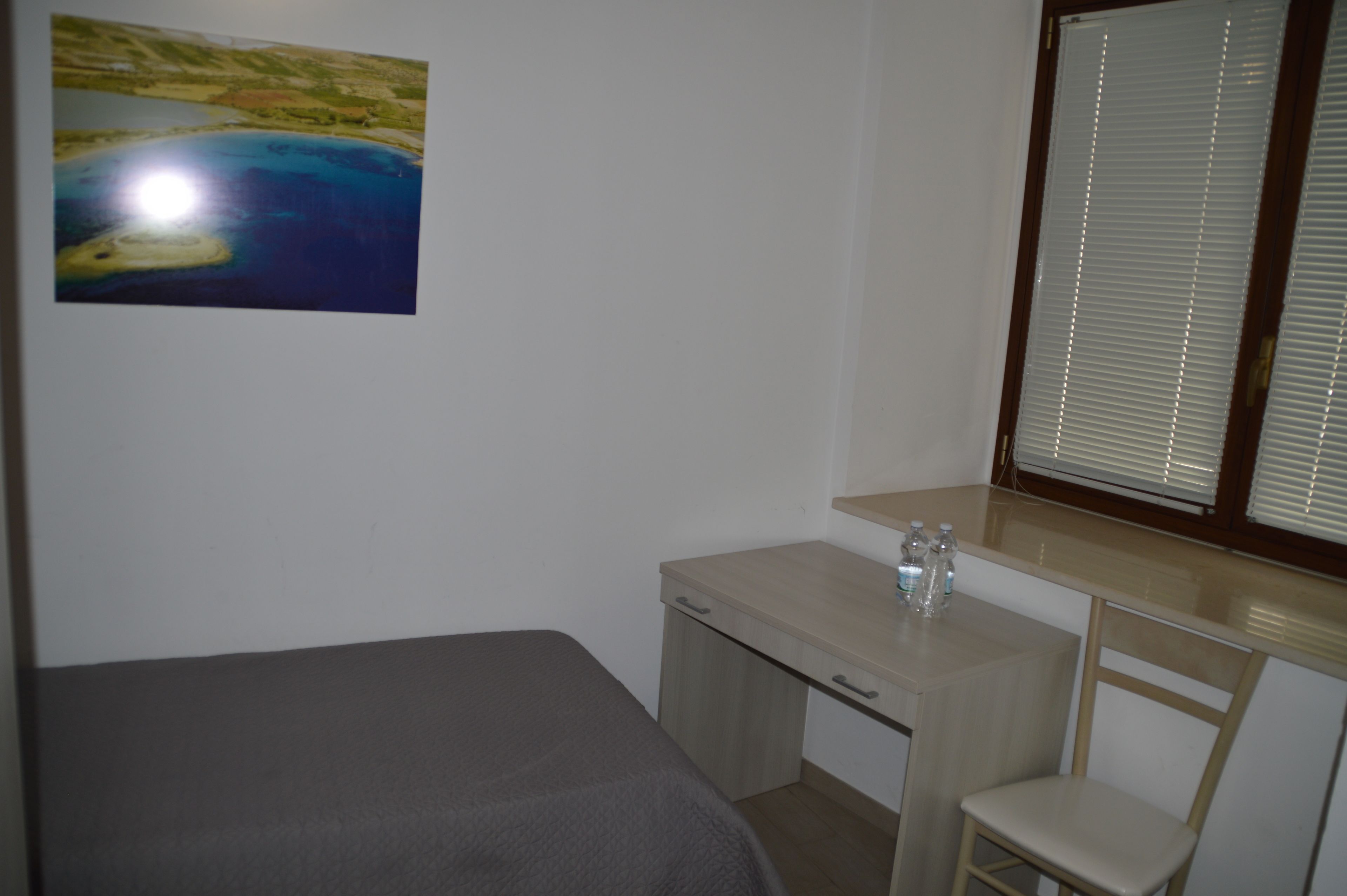 A bedroom with a bed, a desk, a chair, and a window with blinds.