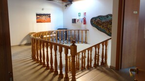 A wooden staircase with a railing, a fire extinguisher, and a wall-mounted emergency exit sign. - Il Veliero (Pachino)