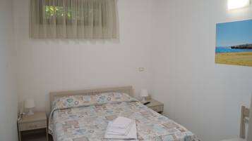 Une chambre à coucher comprenant un lit, deux tables de chevet, une chaise, une fenêtre avec un rideau et un tableau accroché au mur.