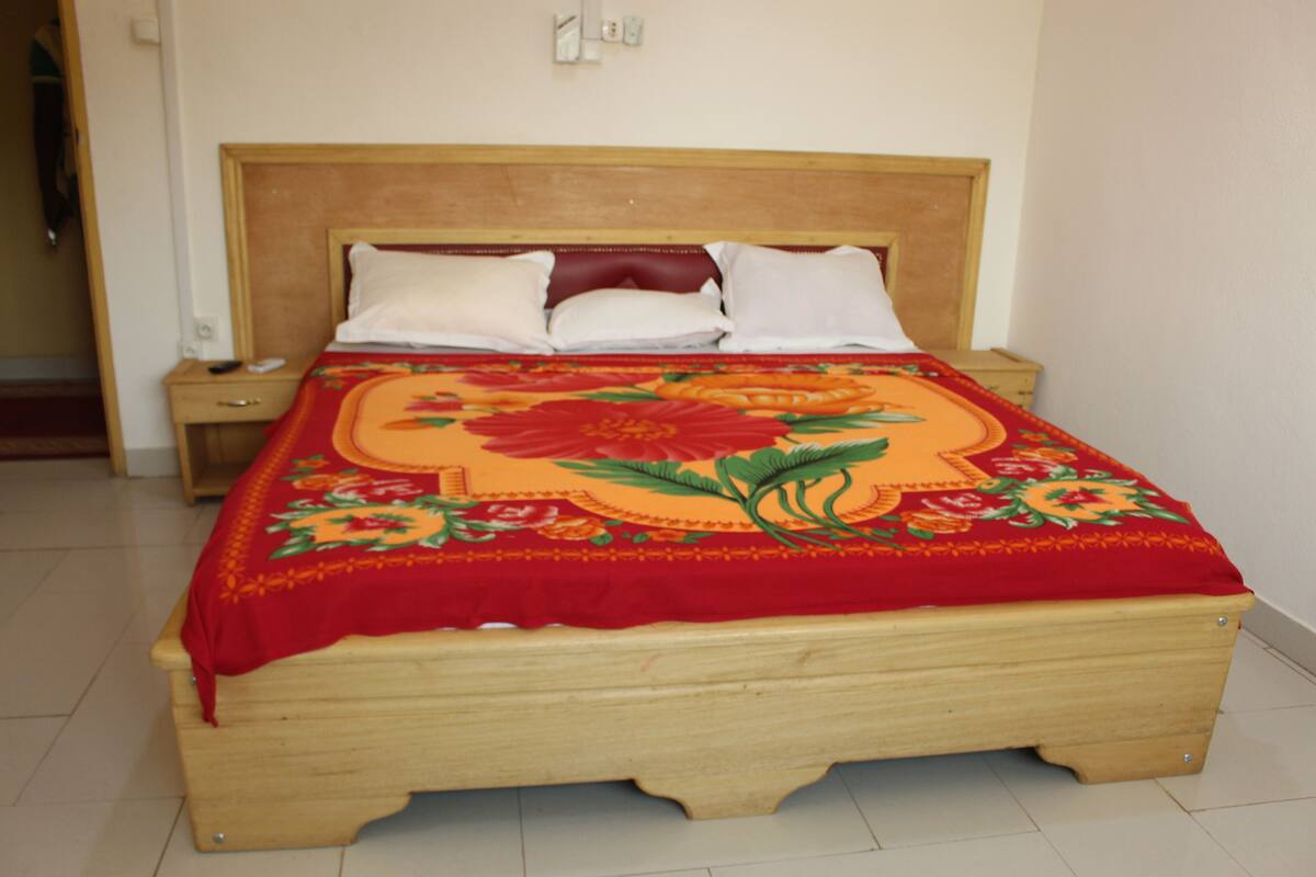 A wooden bed with a floral bedspread, a wooden headboard, and two white pillows.