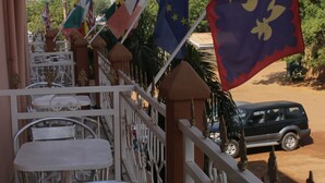 A balcony with metal chairs and tables, flags, and a parked SUV. - Hôtel la Tour d'Argent (Garoua)