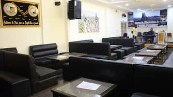 A restaurant with black leather booths and tables, a stage with a piano, and a large mural on the wall.