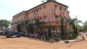 A multi-story building with a balcony, air conditioning units, and multiple flags. - Hôtel la Tour d'Argent (Garoua)