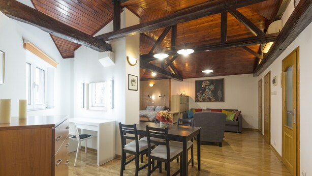 A spacious living area with a wooden ceiling, a dining table with chairs, a sofa, and a kitchen area with a wooden cabinet and a chair. - Belgrade Center Apartment V (Belgrade)