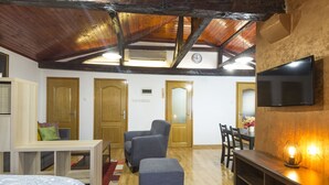 A room with a wooden ceiling, a bed, a sofa, a TV mounted on the wall, and a dining area with chairs and a table. - Belgrade Center Apartment V (Belgrade)