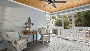 Een overdekt terras met rieten schommelstoelen en een tafel, een houten plafond en uitzicht op de omgeving.