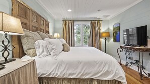 Een slaapkamer met een groot bed, een houten hoofdbord, twee nachtkastjes met lampen, een televisie en een raam met gordijnen.