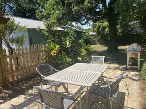An outdoor patio with a table and chairs, a barbecue grill, and a wooden fence.