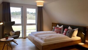 A bedroom with a large bed, a chair, a small table, and a view through the window. - Zollersteighof (Albstadt)