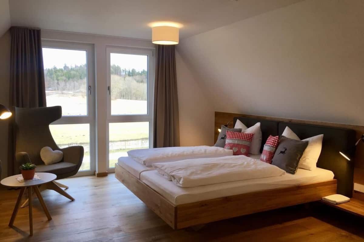 Une chambre avec un grand lit, une chaise, une petite table et une vue par la fenêtre.