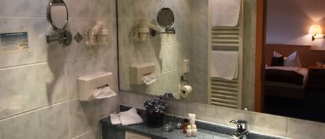 Un baño moderno con pared de azulejos de mármol, lavamanos blanco, espejo y retrete.