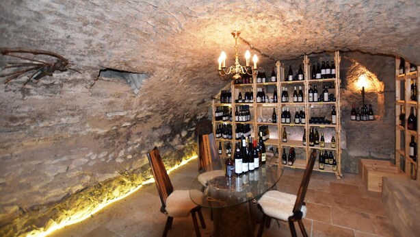 A wine cellar with a round table, chairs, and shelves of wine bottles. - Zollersteighof (Albstadt)