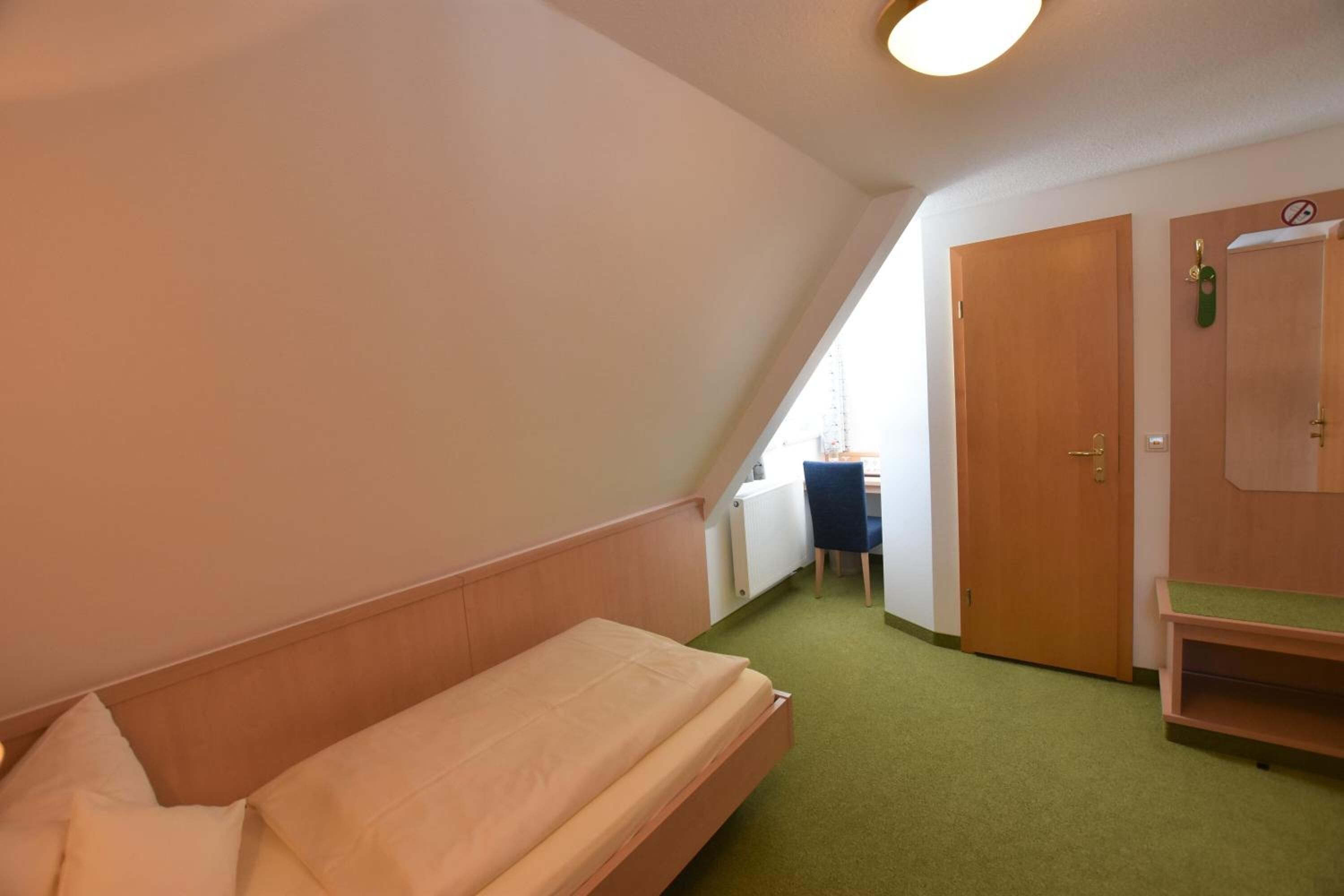 A small, triangular room with a single bed, a desk, and a door.