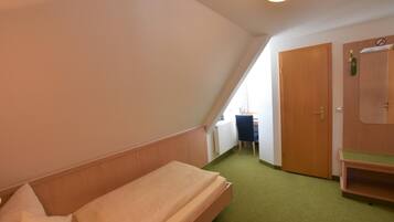 A small, triangular room with a single bed, a desk, and a door.