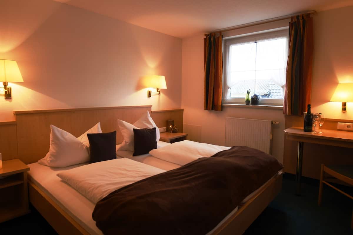 Une chambre d’hôtel comprenant un lit, des lampes de chevet, un bureau avec une chaise, une fenêtre avec des rideaux et un radiateur.