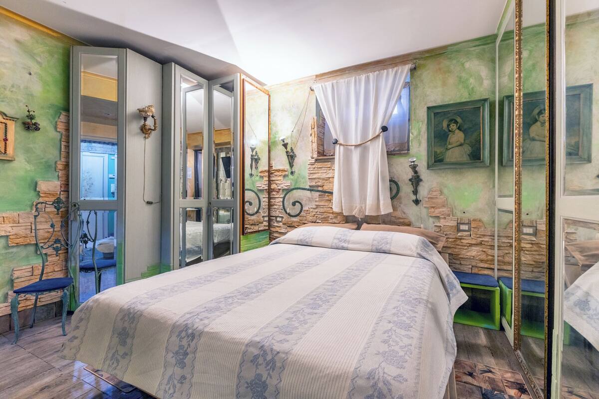 Ein Schlafzimmer mit einem großen Bett, einem Spiegel, einer Bank und einer grünen Wand mit Steinmuster.