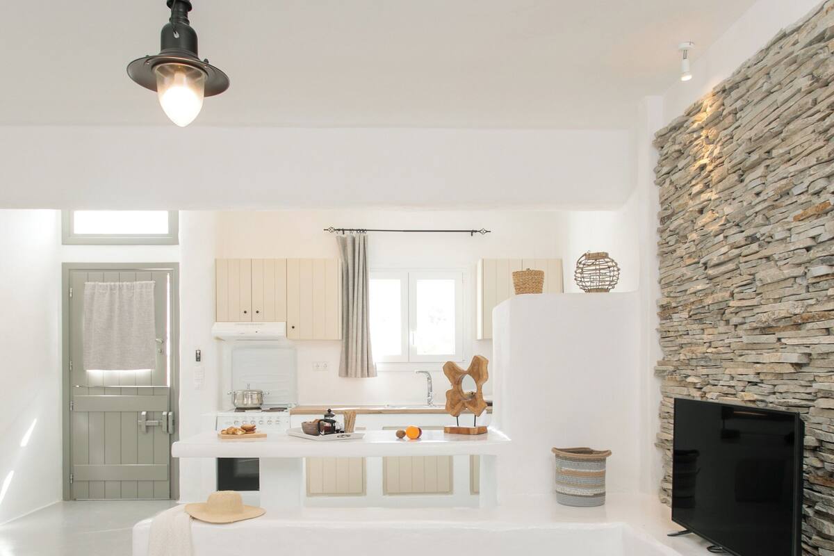 A modern kitchen with white cabinets, a stone accent wall, and a flat-screen TV.