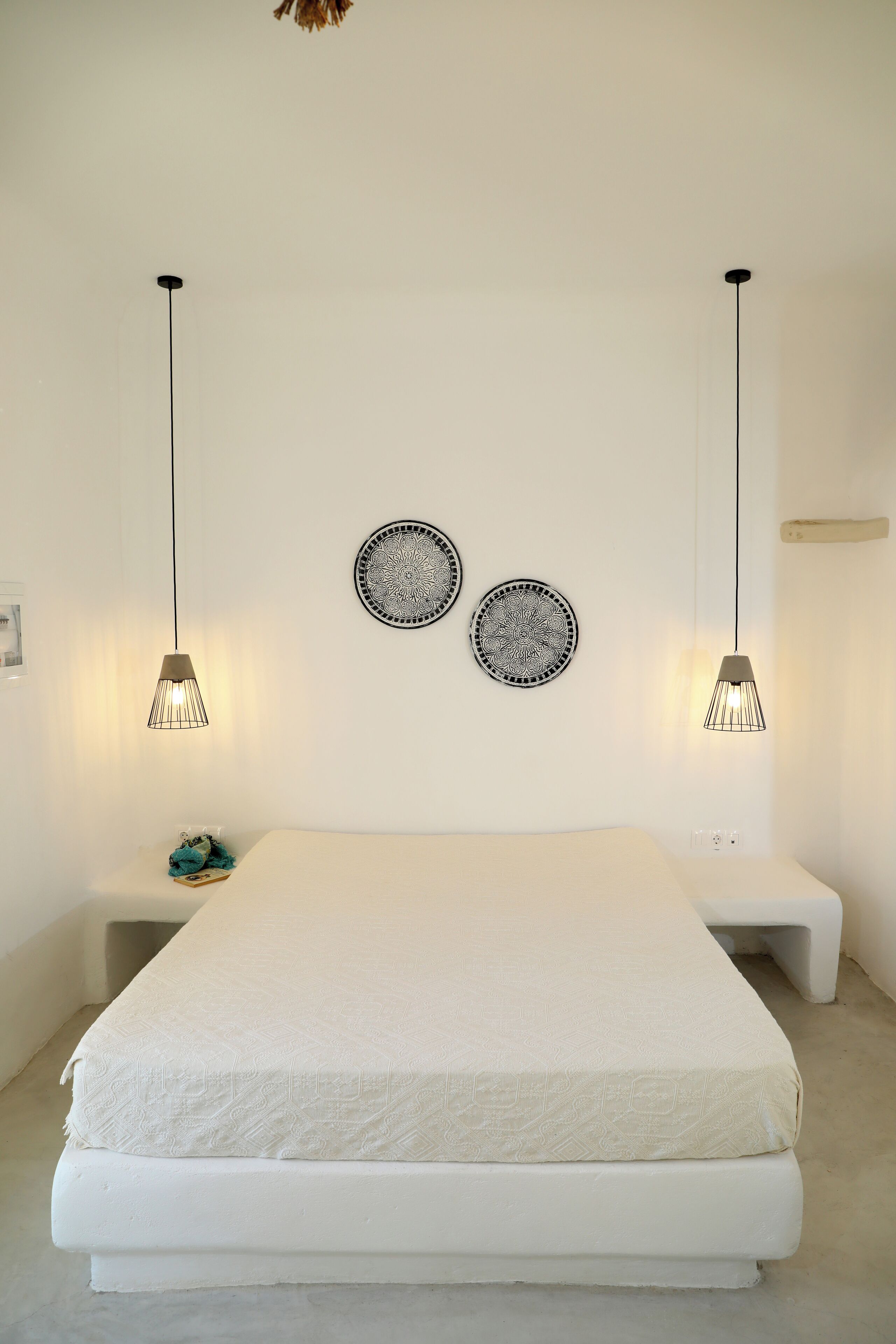 A minimalist bedroom with a large bed, two pendant lights, and two decorative plates on the wall.