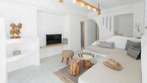 A modern living room with a sofa, a TV, wooden stools, and a decorative hat. - Irida Vacation Suites (Naxos)