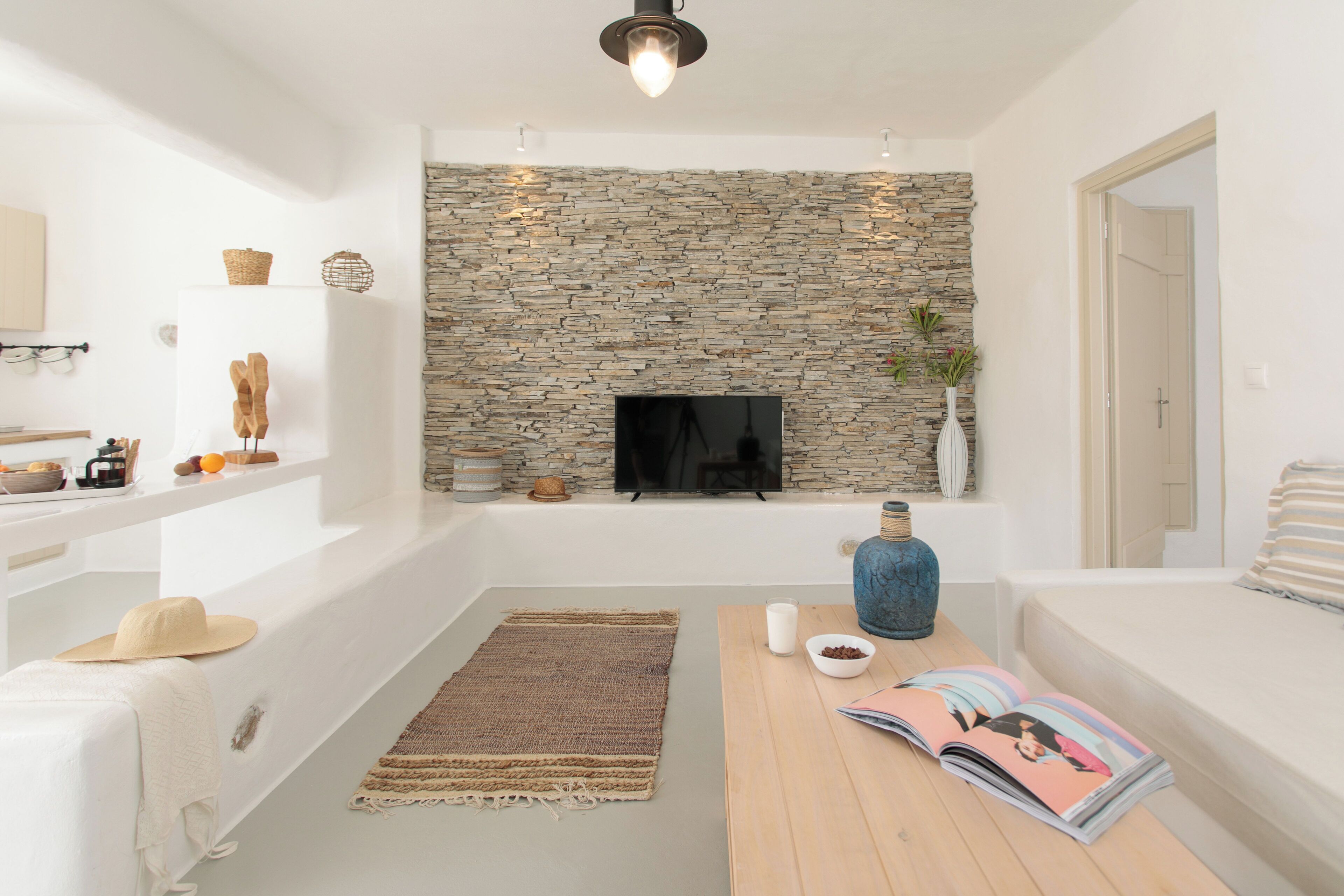A modern living room with a stone wall, a flat-screen TV, a wooden table, and a sofa.