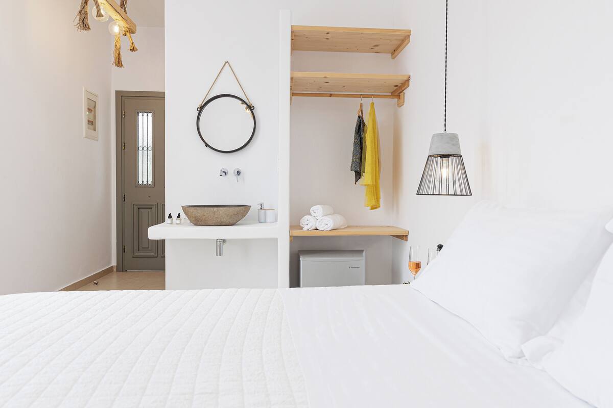 A bedroom with a bed, a wooden shelf with towels, a hanging light fixture, and a door with a window.