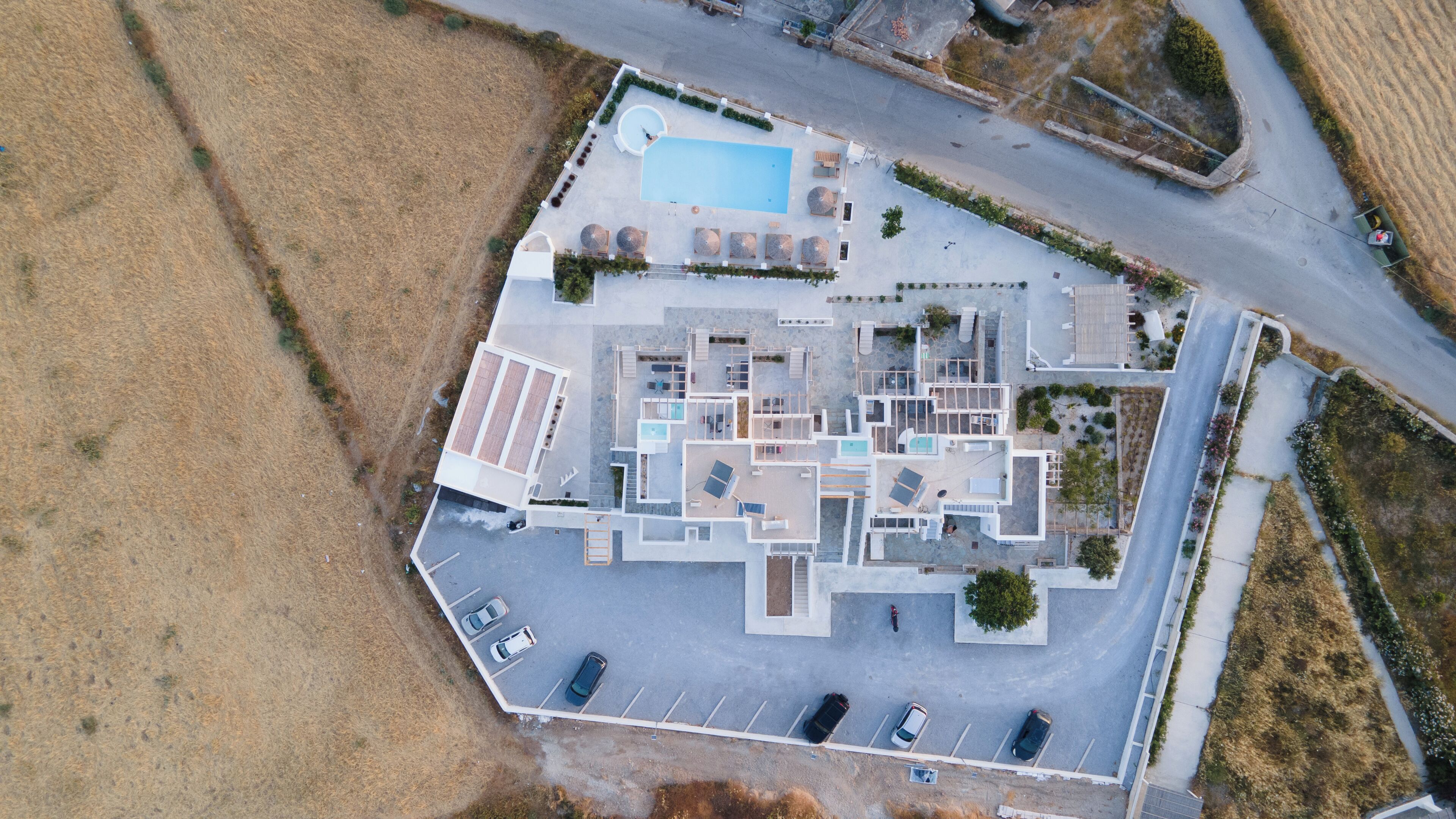 An aerial view of a modern hotel with a swimming pool, multiple rooms, and a parking area.
