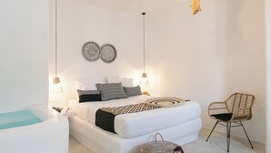 A modern bedroom with a large bed, bedside lamps, a hanging light fixture, and a woven chair. - Irida Vacation Suites (Naxos)