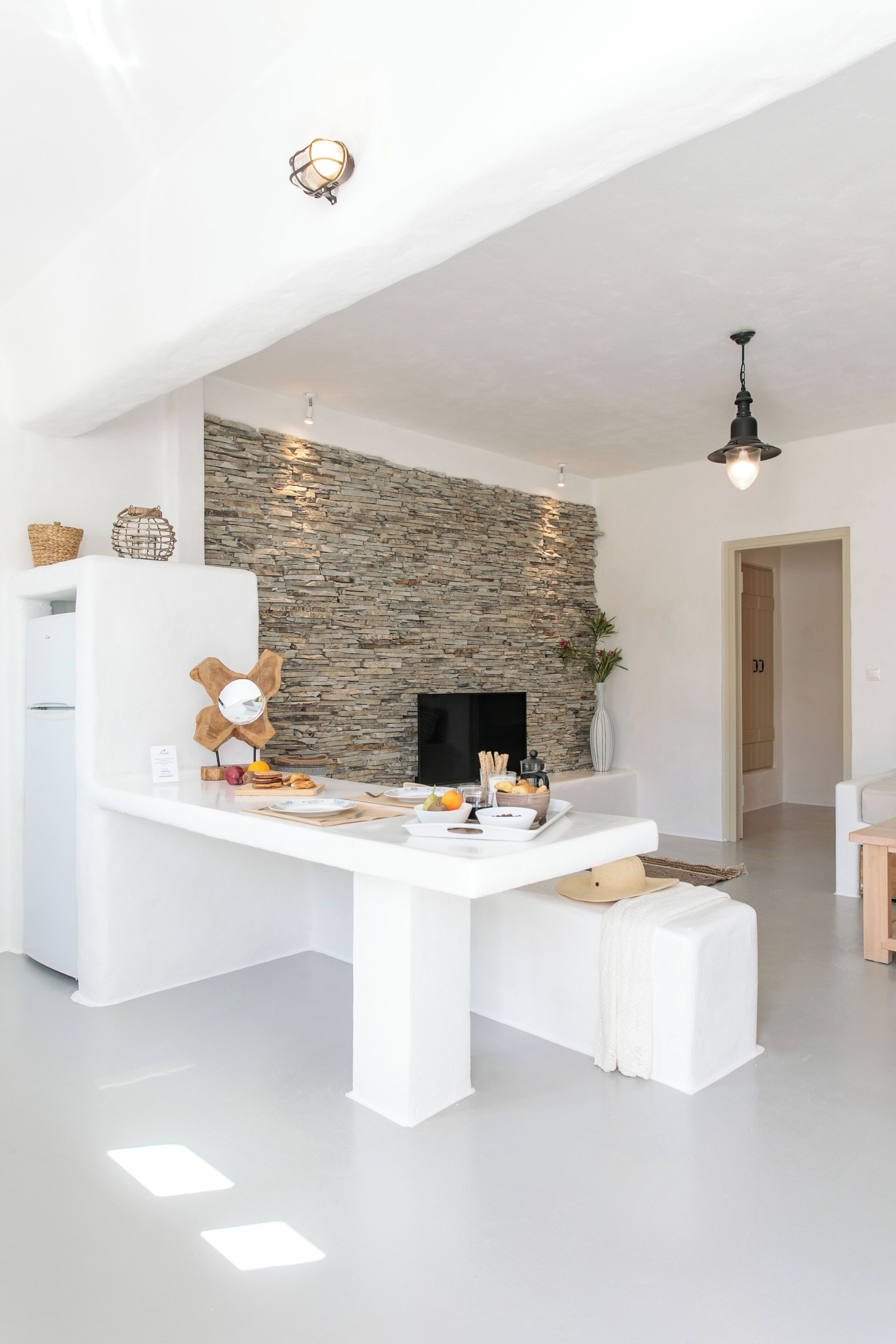 A modern kitchen with a stone wall, white cabinetry, and a central island with a flat-screen TV.
