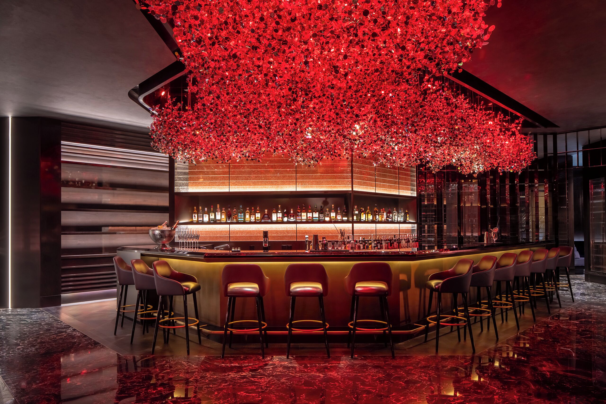 A bar area with a red floral ceiling, a bar counter, and multiple bar stools.