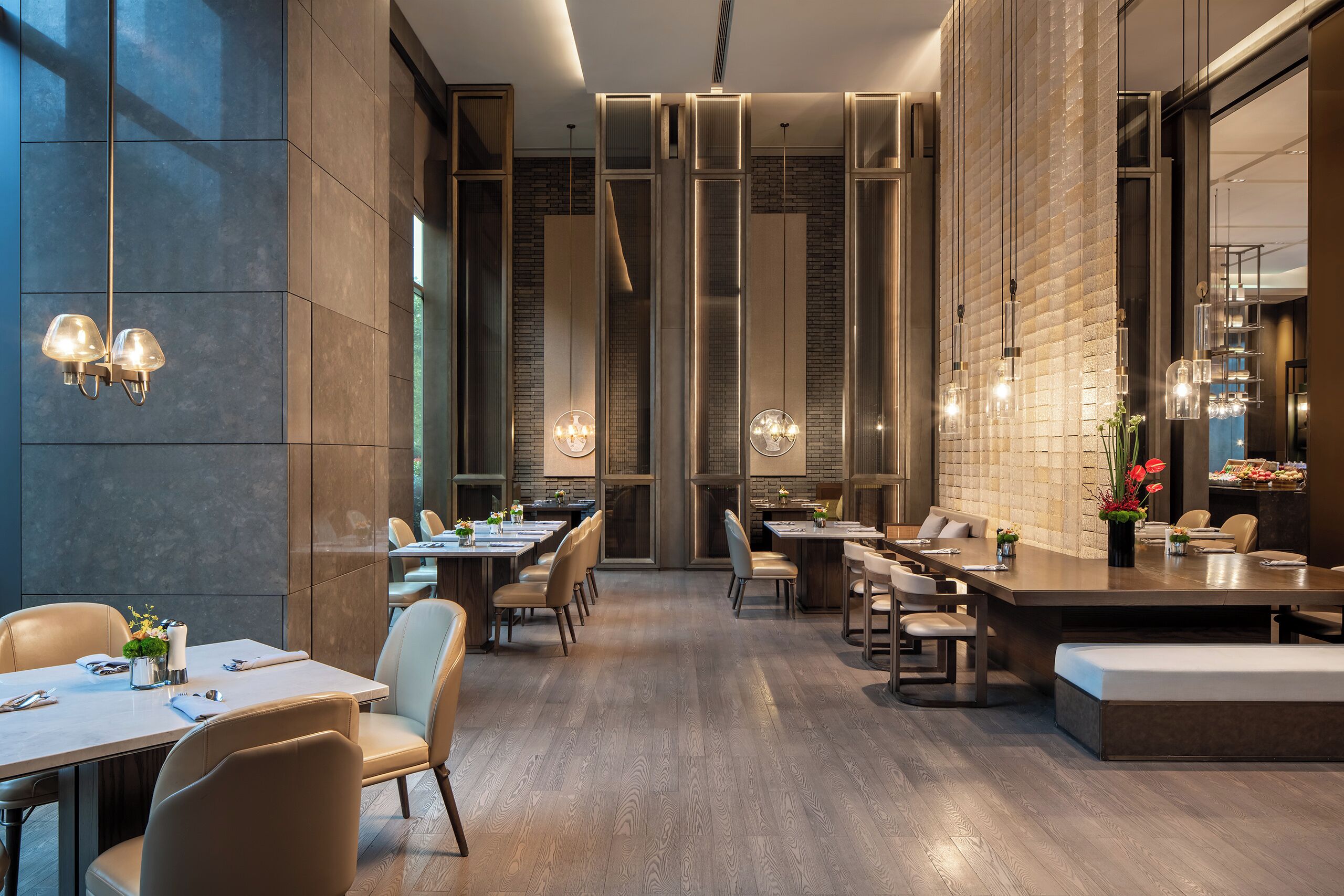 Un restaurante moderno con techos altos, mesas largas y lámparas colgantes.
