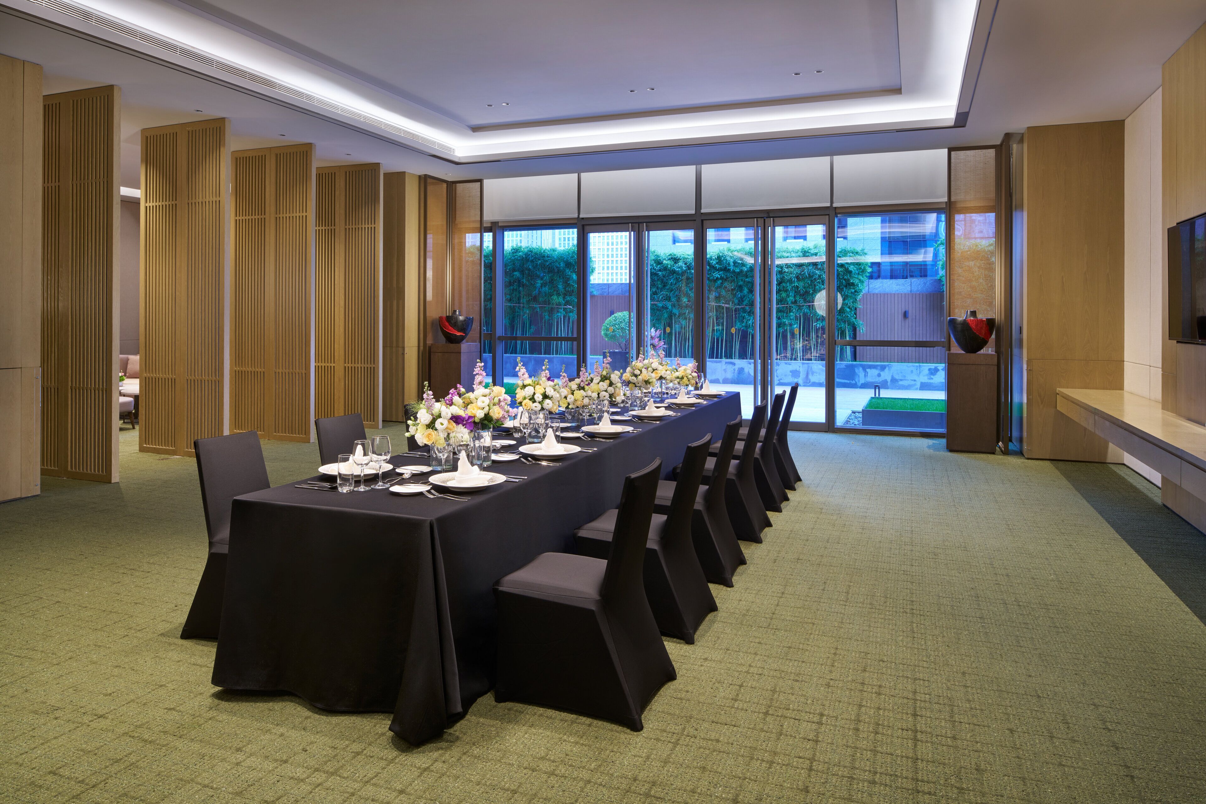 A conference room with a long table set for a meeting, large windows, and a television on the wall.