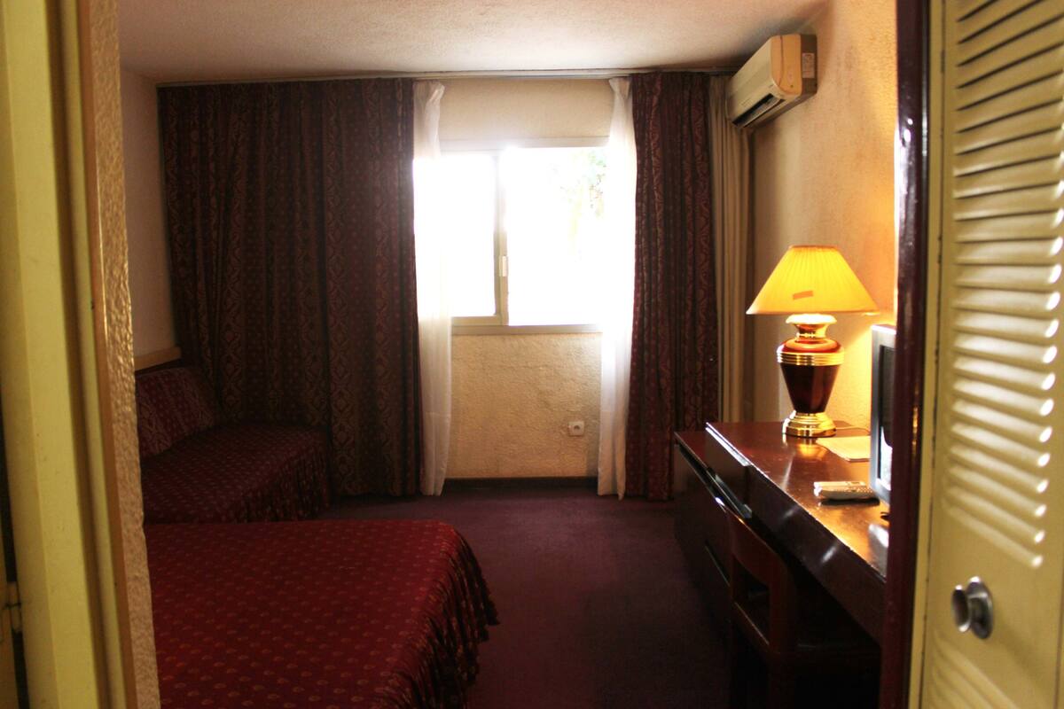 Habitación de hotel con dos camas, un escritorio, una lámpara y una ventana con cortinas.