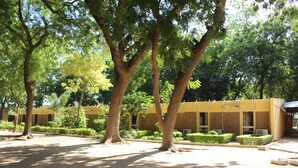 A courtyard with trees and a yellow building with air conditioning units. - Hotel Mizao (Maroua)