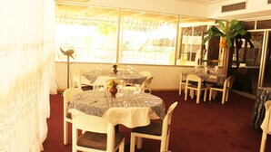 A dining area with tables set for four, white chairs, and a large window providing a view of the outdoors. - Hotel Mizao (Maroua)