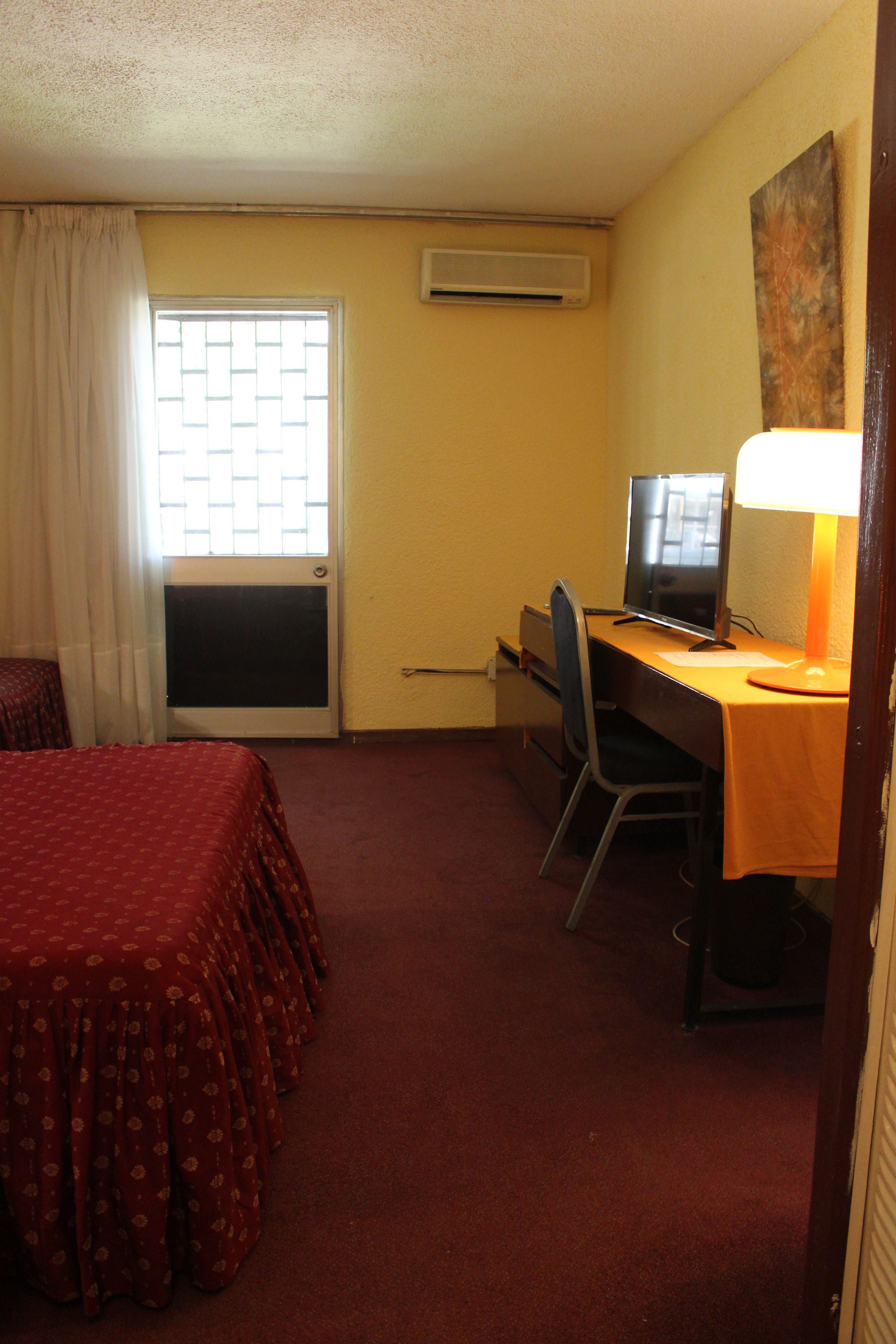 Una habitación de hotel con cama, escritorio con computadora, silla y ventana con cortinas.