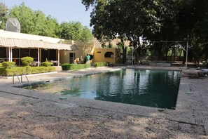 Une piscine avec une terrasse carrelée, une antenne parabolique sur un bâtiment et un espace couvert avec des sièges.