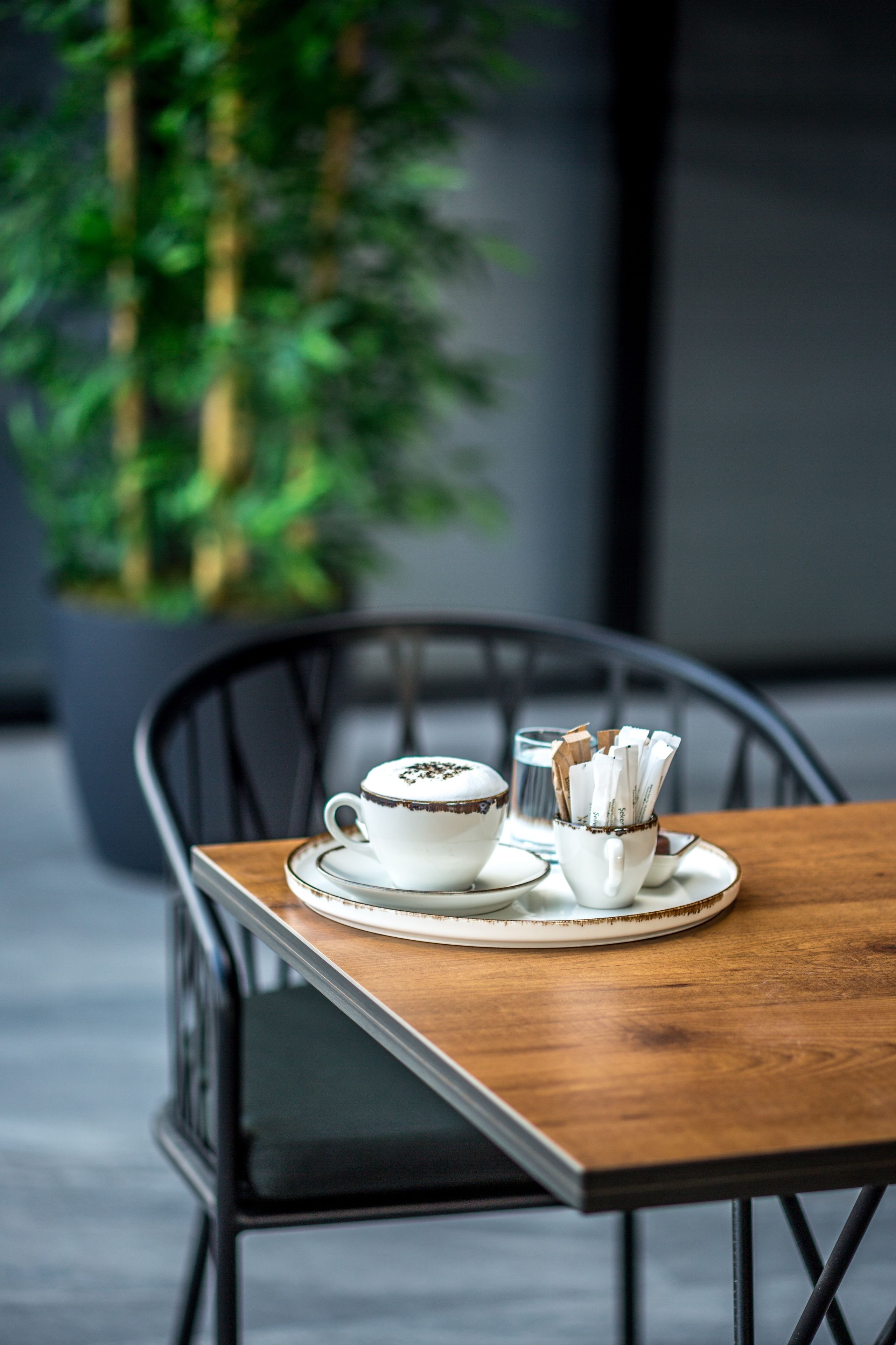 A table with a white cup and saucer, a glass, and a napkin holder on a wooden table.