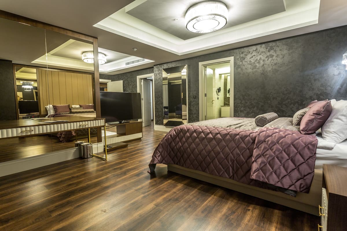A modern bedroom with a large bed, a TV, a mirror, and a wooden floor.