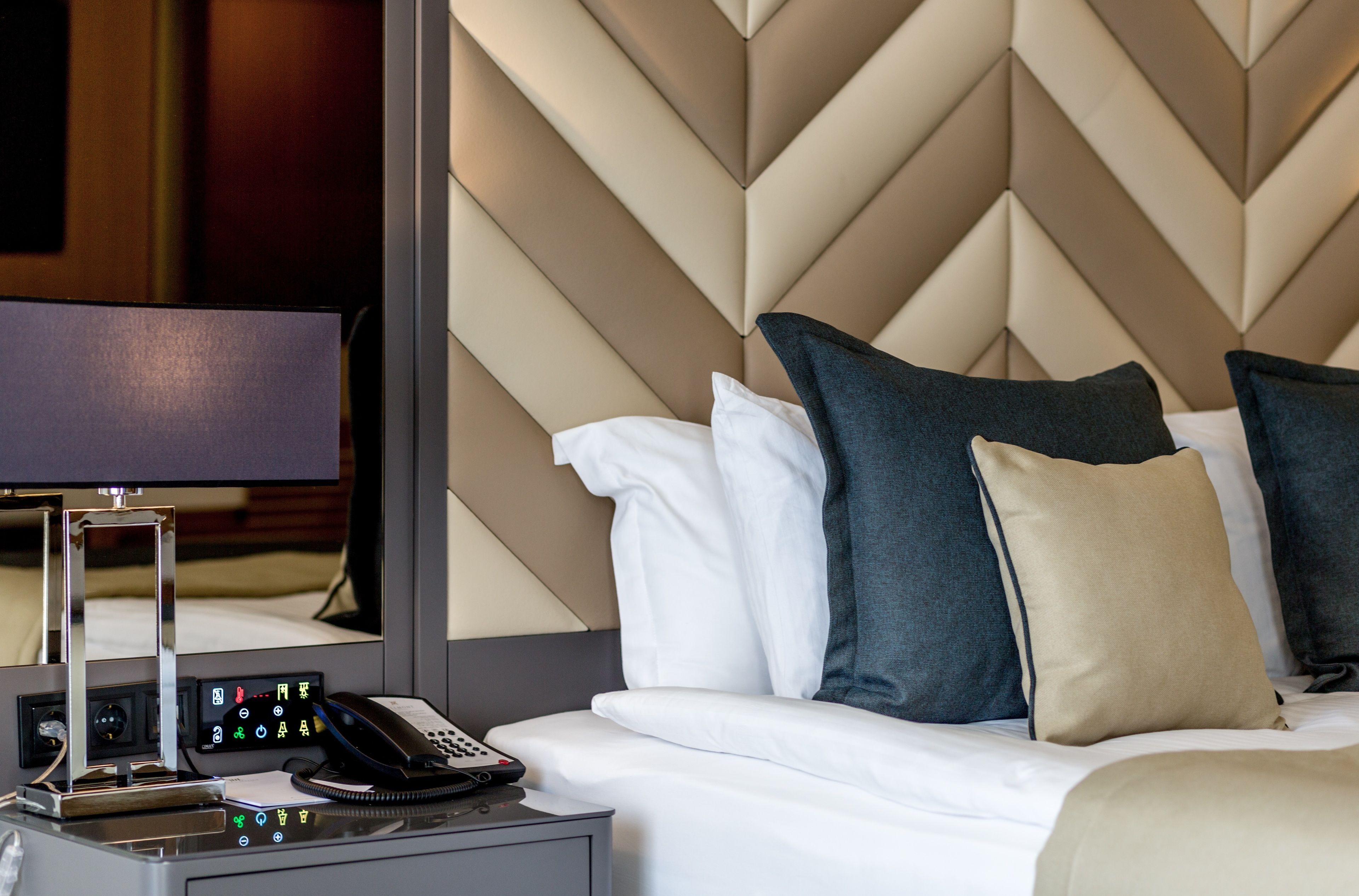Une chambre d’hôtel avec un lit, une table de chevet dotée d’un téléphone et d’une lampe, et un mur orné d’un motif géométrique.